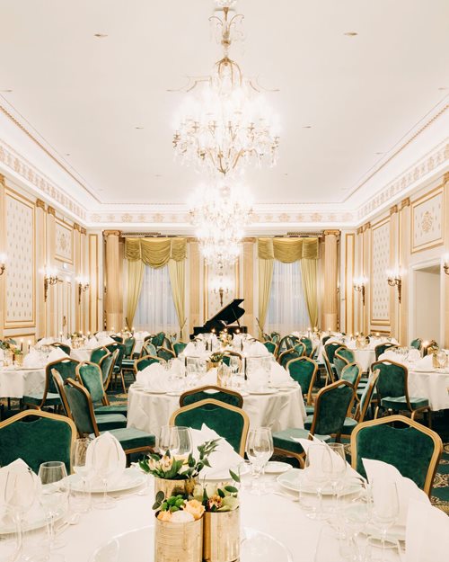 Bright banqueting area with decorated tables, green delicate chairs and chandeliers hanging from the ceiling 